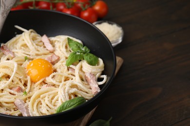 Bowl of delicious pasta Carbonara with egg yolk on wooden table, closeup. Space for text