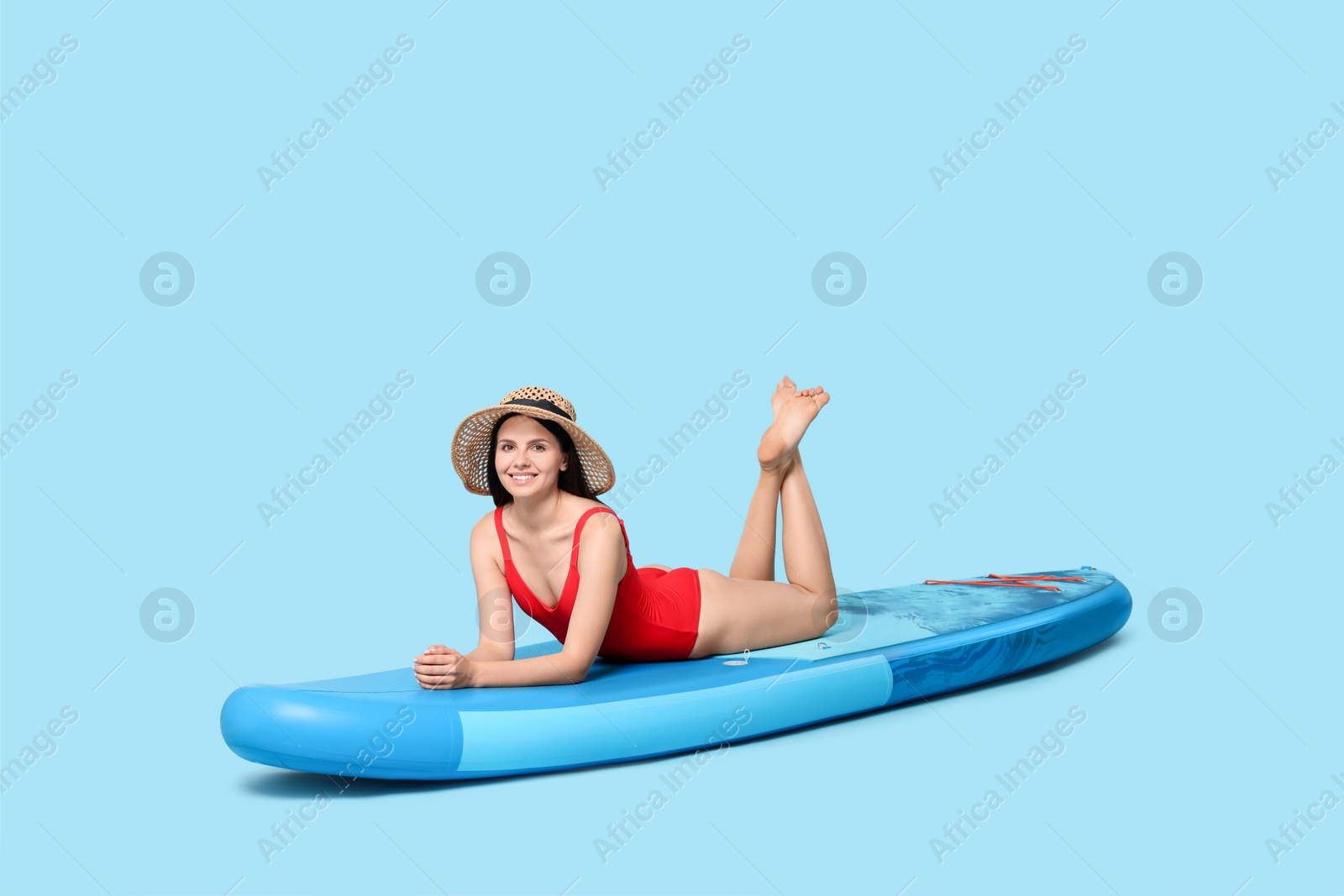 Photo of Happy woman resting on SUP board against light blue background