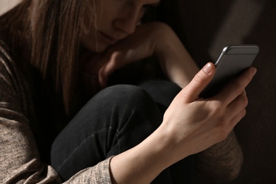Photo of Sad woman using smartphone in dark room, closeup. Loneliness concept