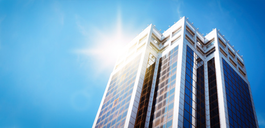 Image of Modern skyscraper with tinted windows against blue sky, low angle view. Building corporation