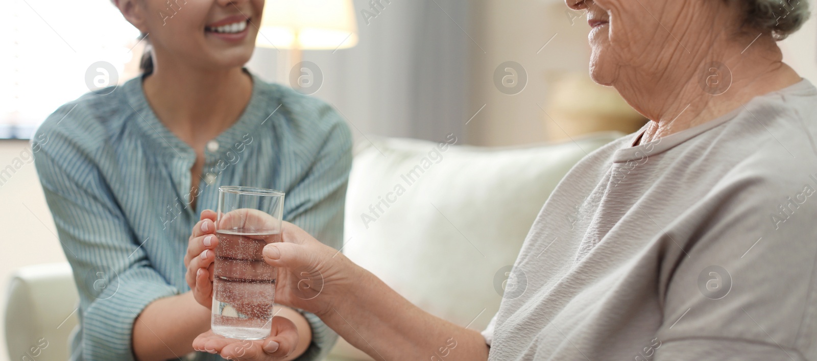 Image of Young woman giving water to elderly lady indoors, banner design. Senior people care