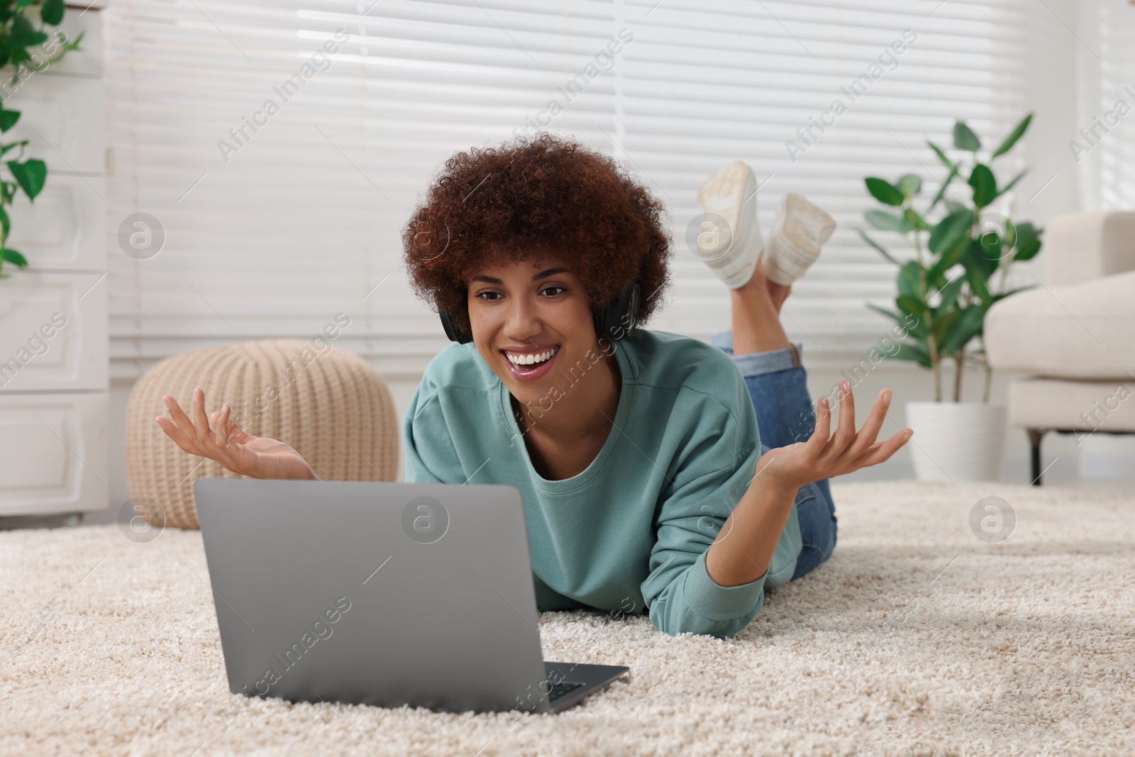 Photo of Beautiful young woman in headphones having video chat via laptop in room