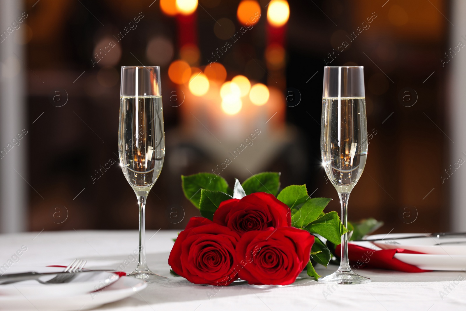 Photo of Romantic dinner table setting with glasses of champagne and red roses in restaurant