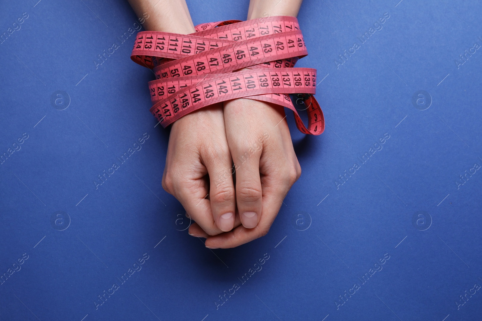 Photo of Woman tied with measuring tape on blue background, top view. Diet concept