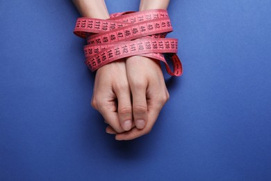 Woman tied with measuring tape on blue background, top view. Diet concept