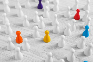 Photo of Colorful pawns on white wooden table. Social inclusion concept