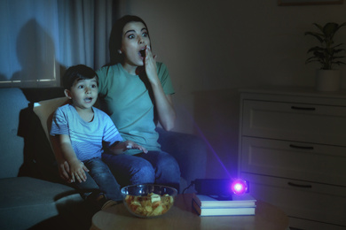 Emotional young woman and her son watching movie using video projector at home. Space for text