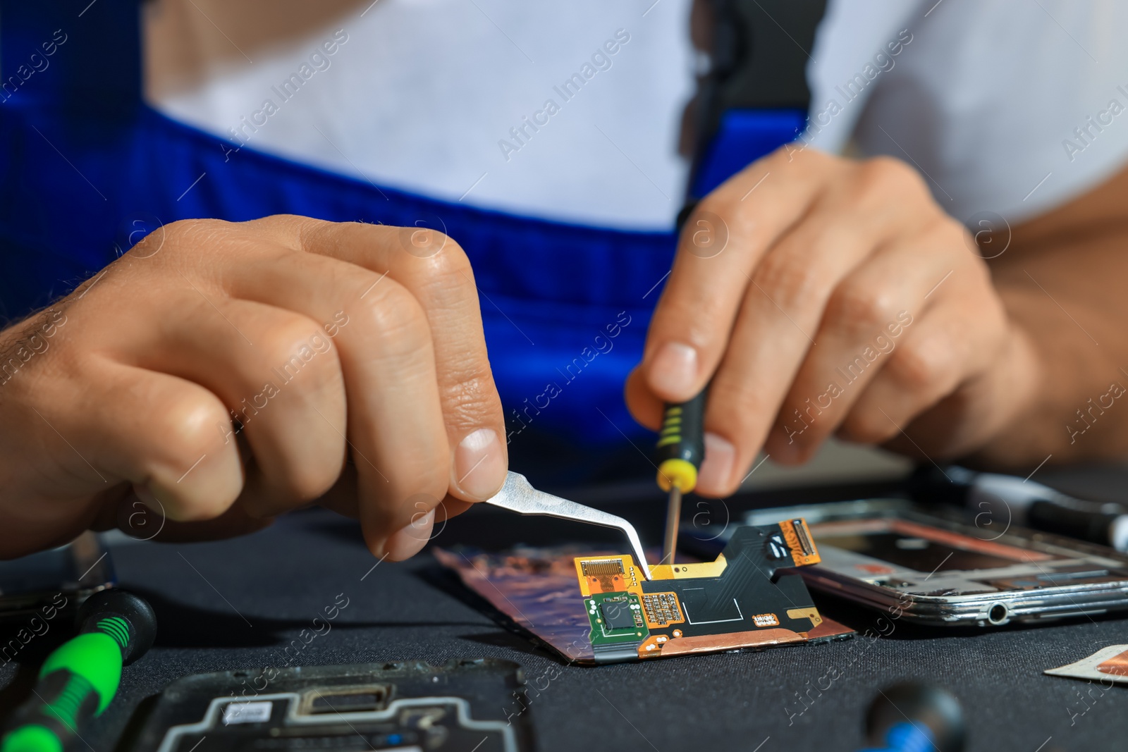 Photo of Technician repairing broken smartphone at table, closeup