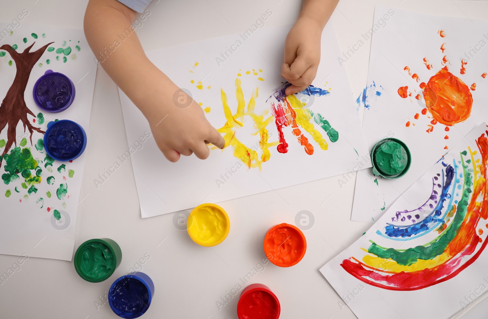 Photo of Little child painting with finger at white table, top view