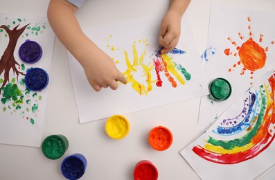 Photo of Little child painting with finger at white table, top view