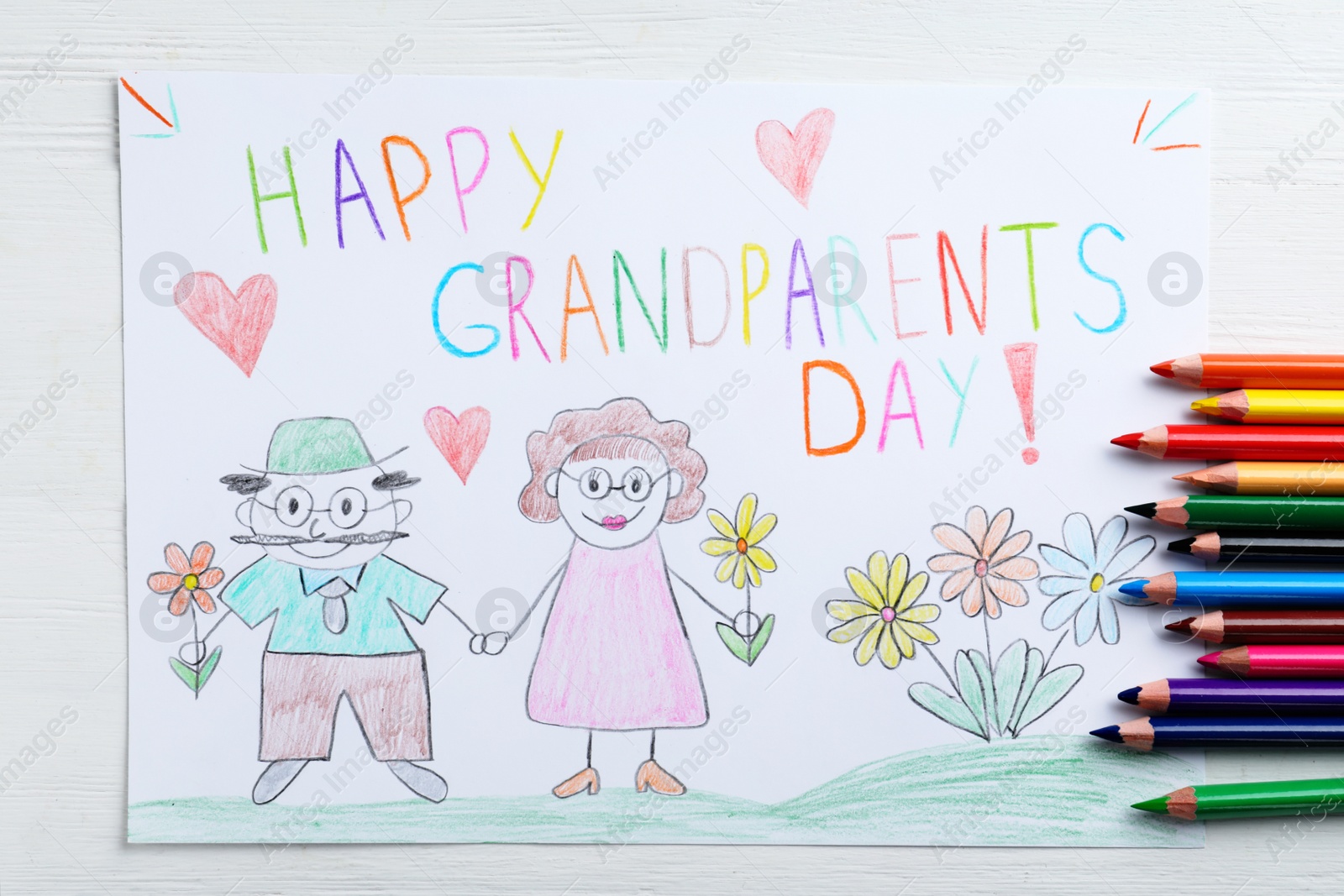 Photo of Beautiful drawing with phrase Happy Grandparents Day on white wooden table, flat lay