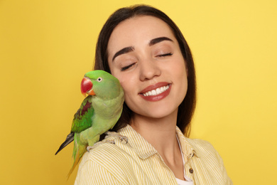 Young woman with Alexandrine parakeet on yellow background. Cute pet