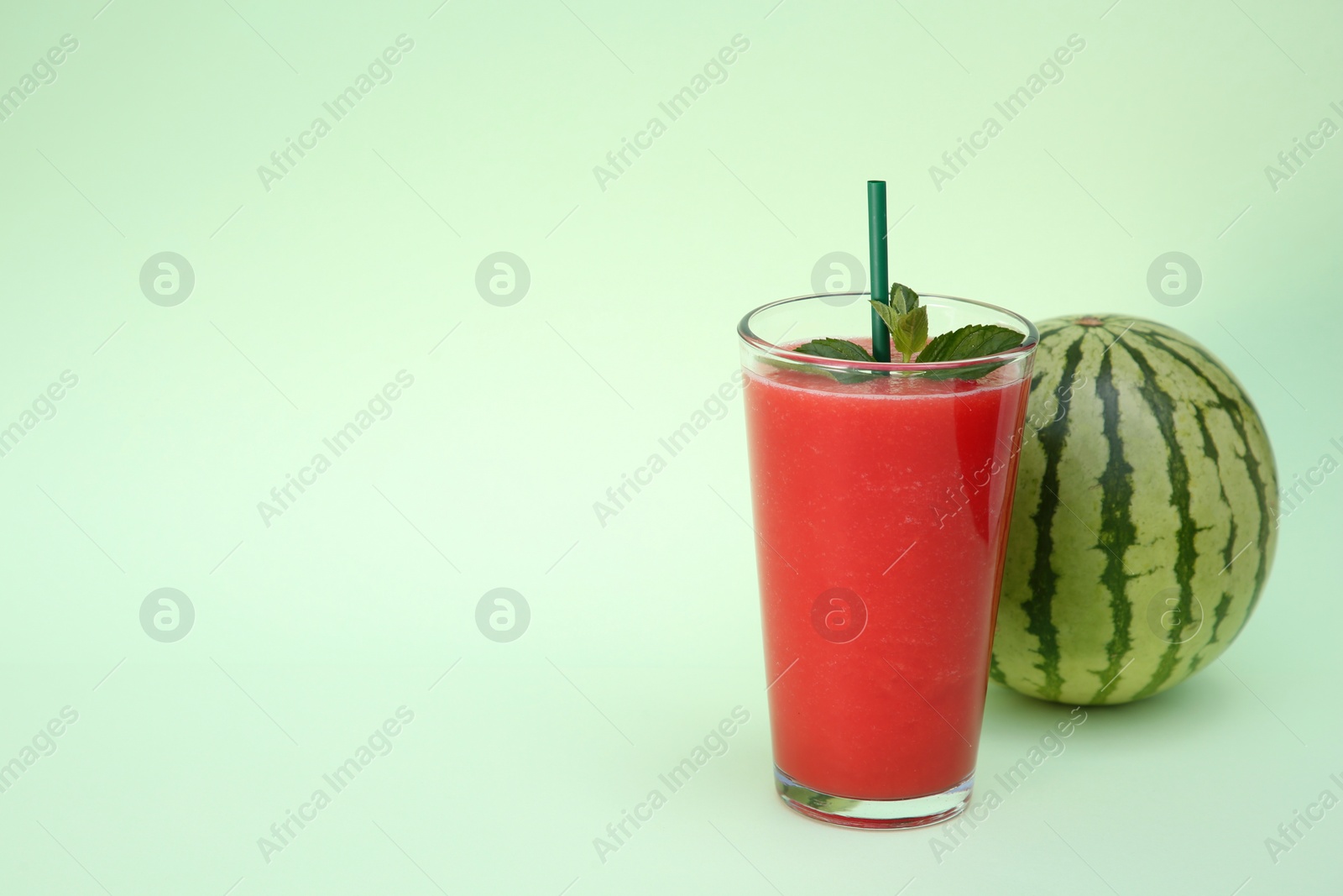 Photo of Glass of delicious drink with mint and fresh watermelon on light green background, space for text