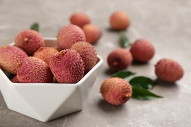 Fresh ripe lychee fruits in ceramic bowl on grey table. Space for text