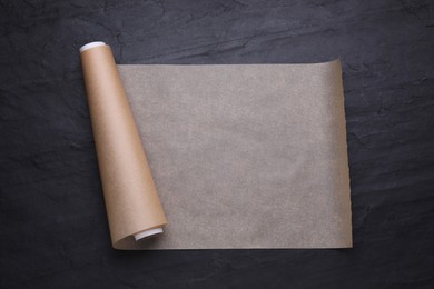 Roll of baking paper on black table, top view
