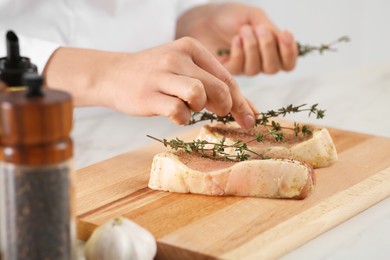 Photo of Professional chef decorating delicious meat with thyme at white table, closeup