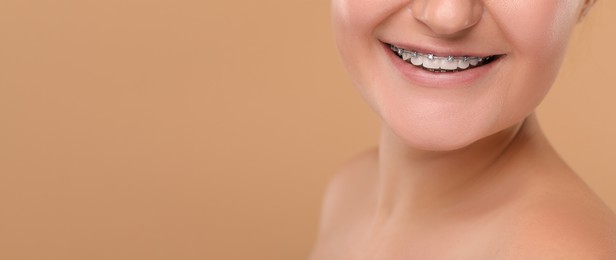 Image of Smiling woman with braces on beige background, closeup. Banner design with space for text