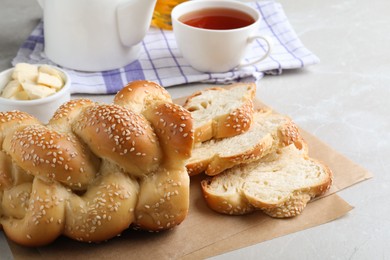 Photo of Cut homemade braided bread and freshly brewed tea on light grey table, closeup. Traditional Shabbat challah
