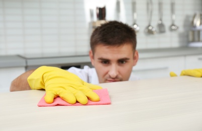 Photo of Man cleaning table with rag in kitchen