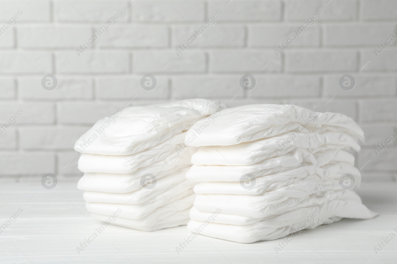 Photo of Baby diapers on wooden table against white brick wall
