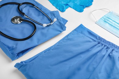 Photo of Medical uniform, stethoscope, face mask and rubber gloves on white background, closeup view