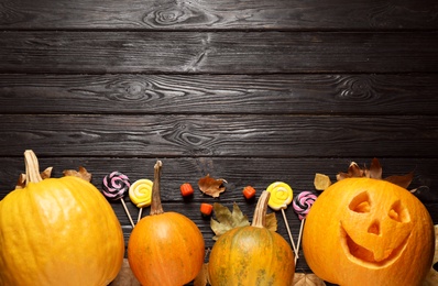 Flat lay composition with pumpkin head Jack lantern and Halloween treats on black wooden background. Space for text