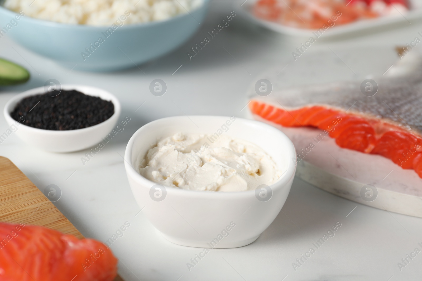 Photo of Cream cheese in bowl and other ingredients for sushi on white table, closeup