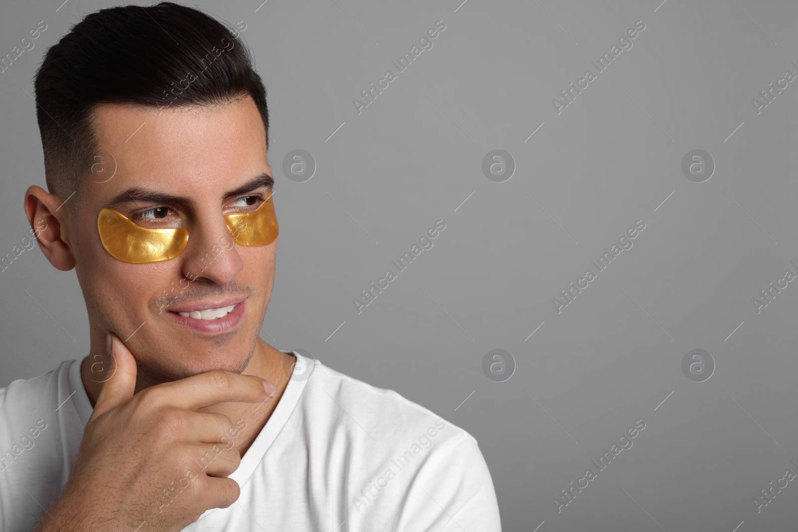 Photo of Man with golden under eye patches on grey background. Space for text