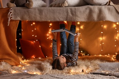 Photo of Girl reading book in decorated play tent at home