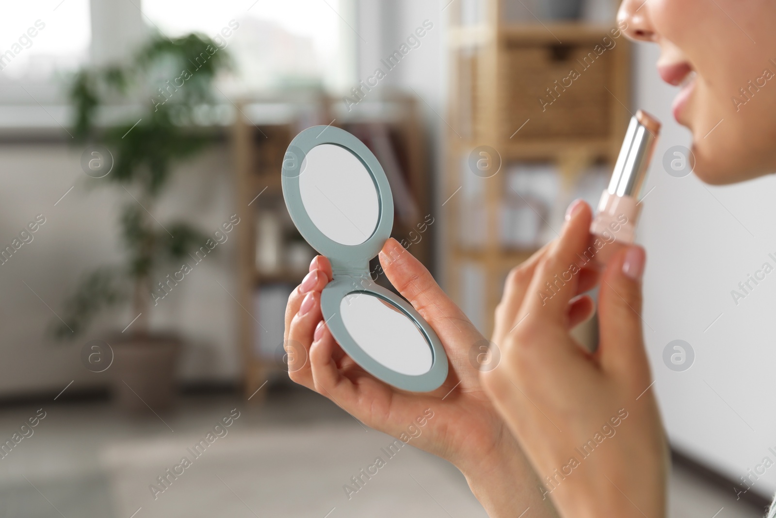 Photo of Young woman using cosmetic pocket mirror while applying make up indoors, closeup