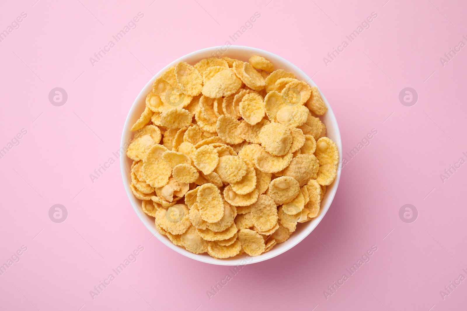 Photo of Breakfast cereal. Tasty corn flakes in bowl on pink table, top view