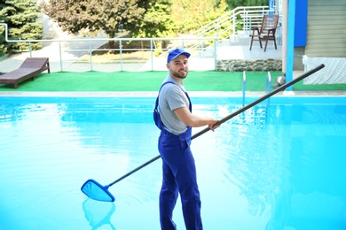 Photo of Male worker cleaning outdoor pool with scoop net