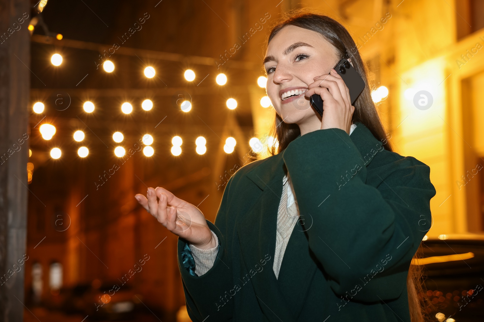 Photo of Smiling woman talking by smartphone on night city street. Space for text