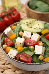 Photo of Bowl of tasty salad with tofu and vegetables on wicker mat, closeup