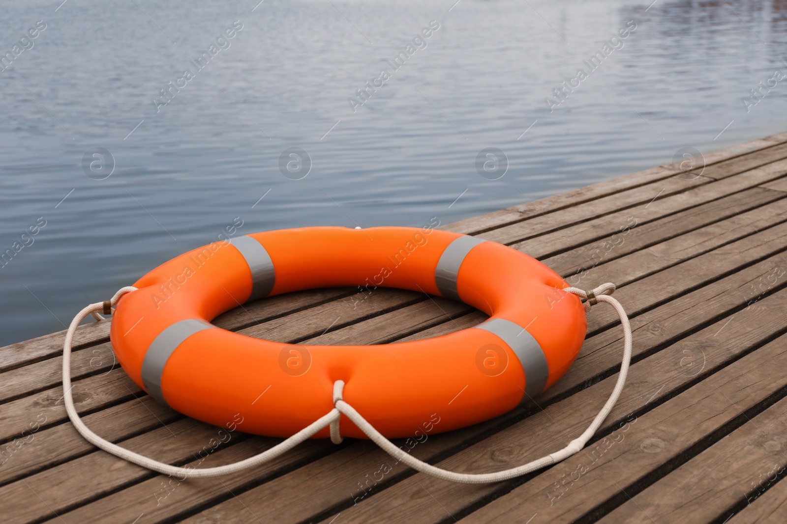 Photo of Orange lifebuoy on wooden pier near water. Rescue equipment