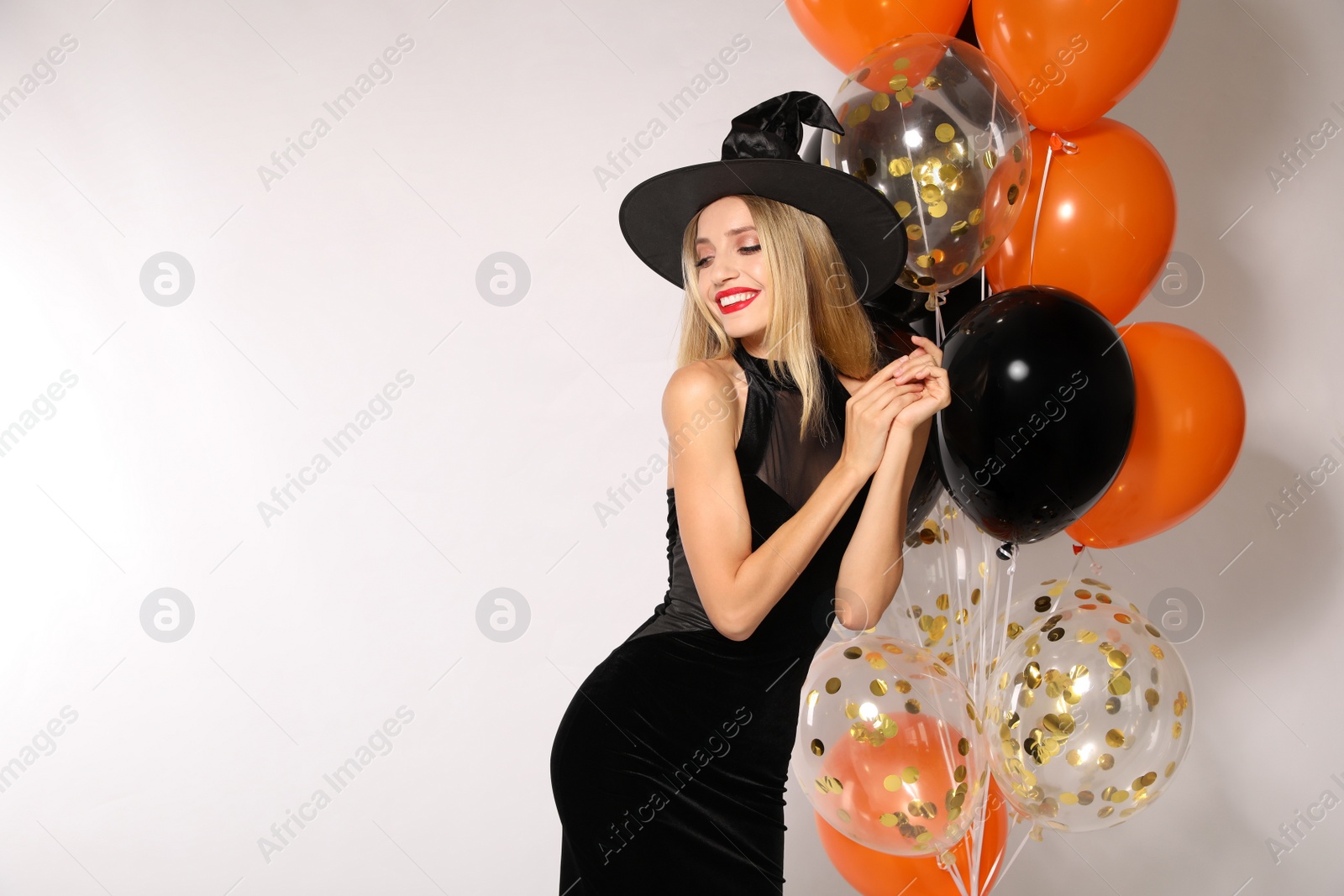 Photo of Beautiful woman in witch costume with balloons on white background, space for text. Halloween party