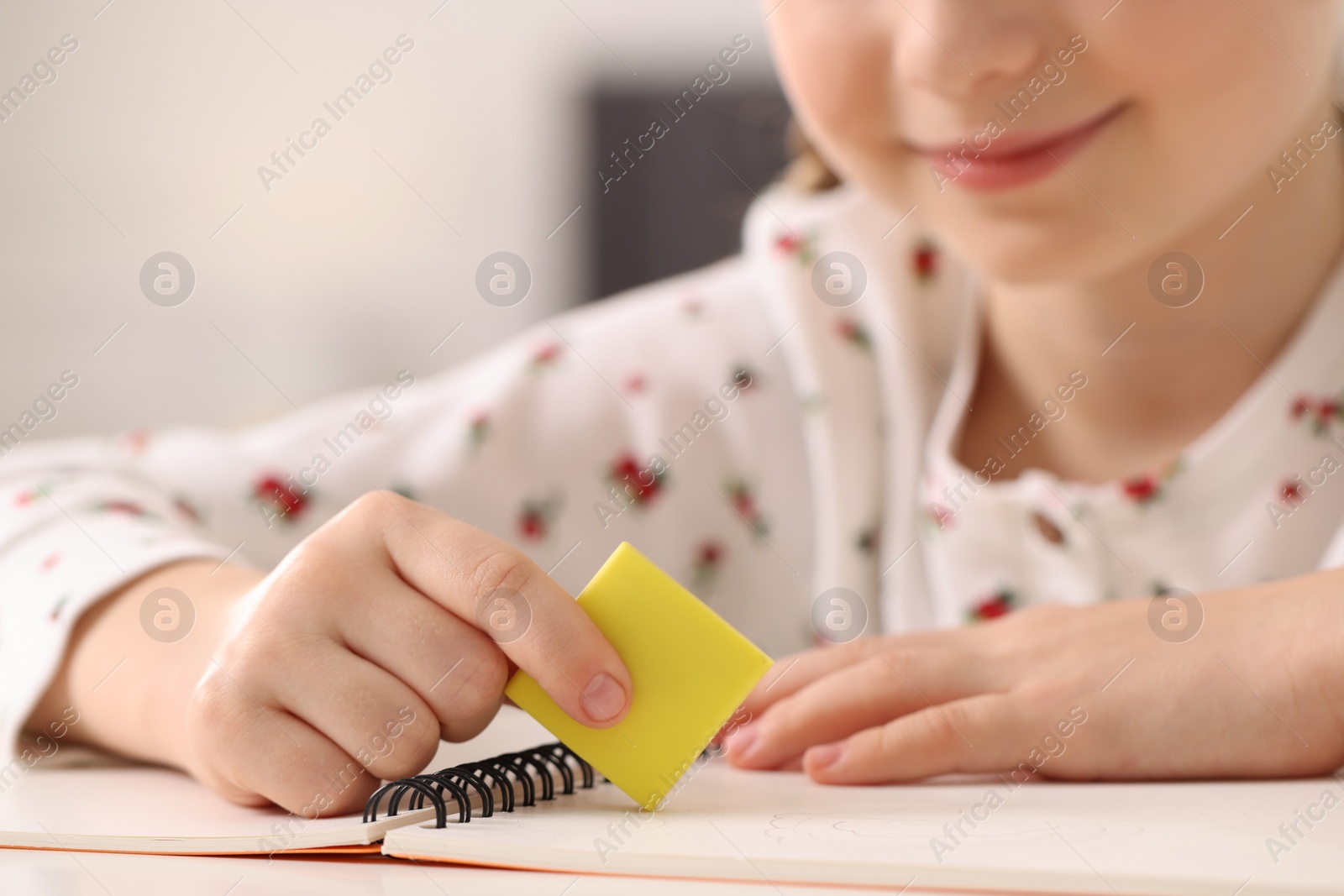 Photo of Girl using eraser at white desk indoors, closeup