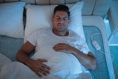 Photo of Man sleeping on electric heating pad in bed at night, above view