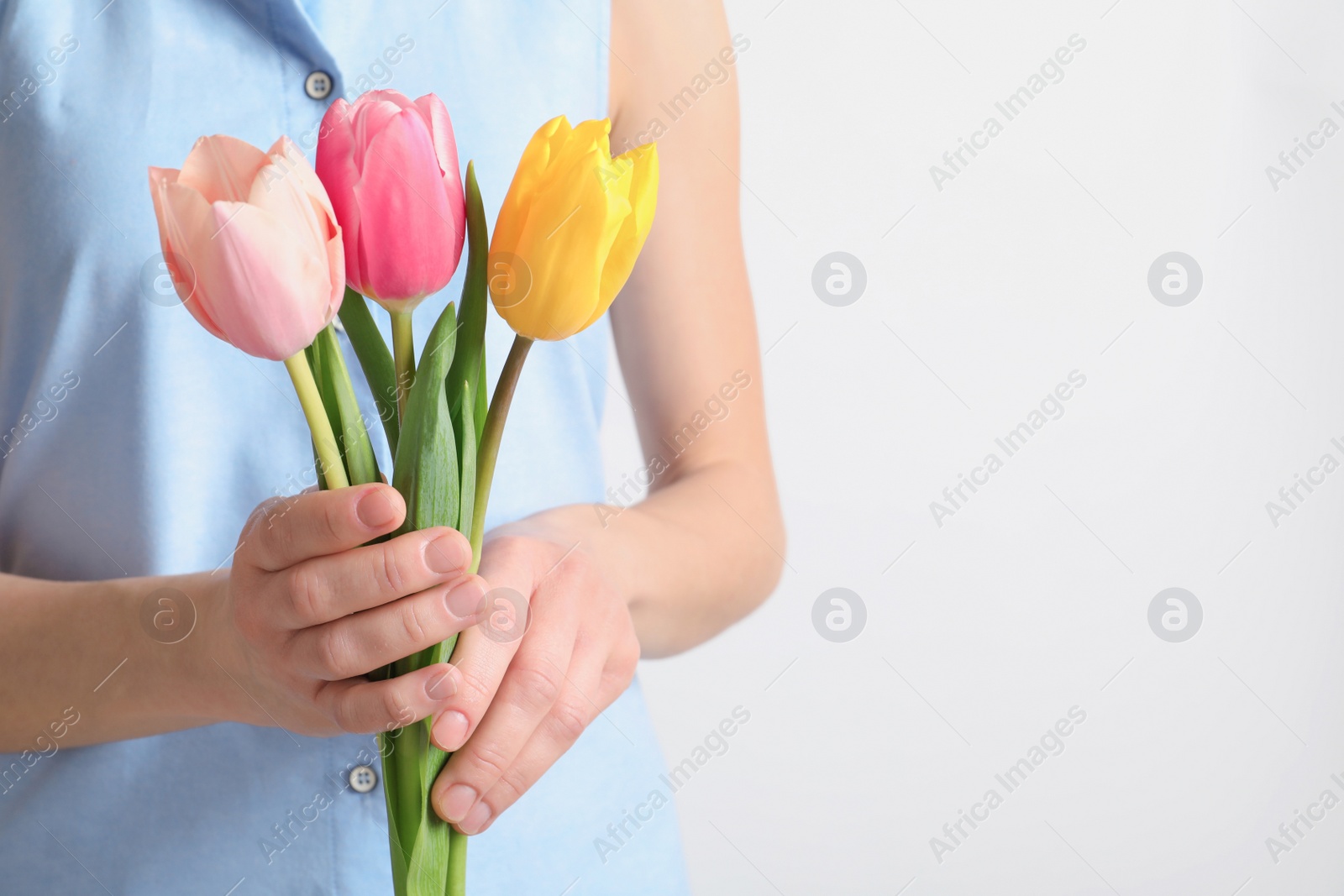 Photo of Girl holding beautiful spring tulips on light background, closeup. International Women's Day