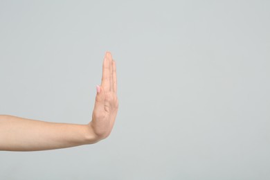 Photo of Woman showing stop gesture on light grey background, closeup. Space for text