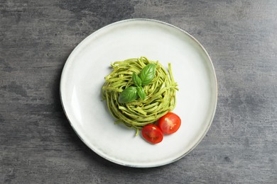 Photo of Tasty tagliatelle with spinach and tomatoes served on grey table, top view. Exquisite presentation of pasta dish