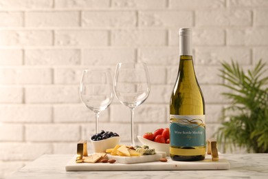 Bottle of wine, glasses and delicious snacks on white marble table