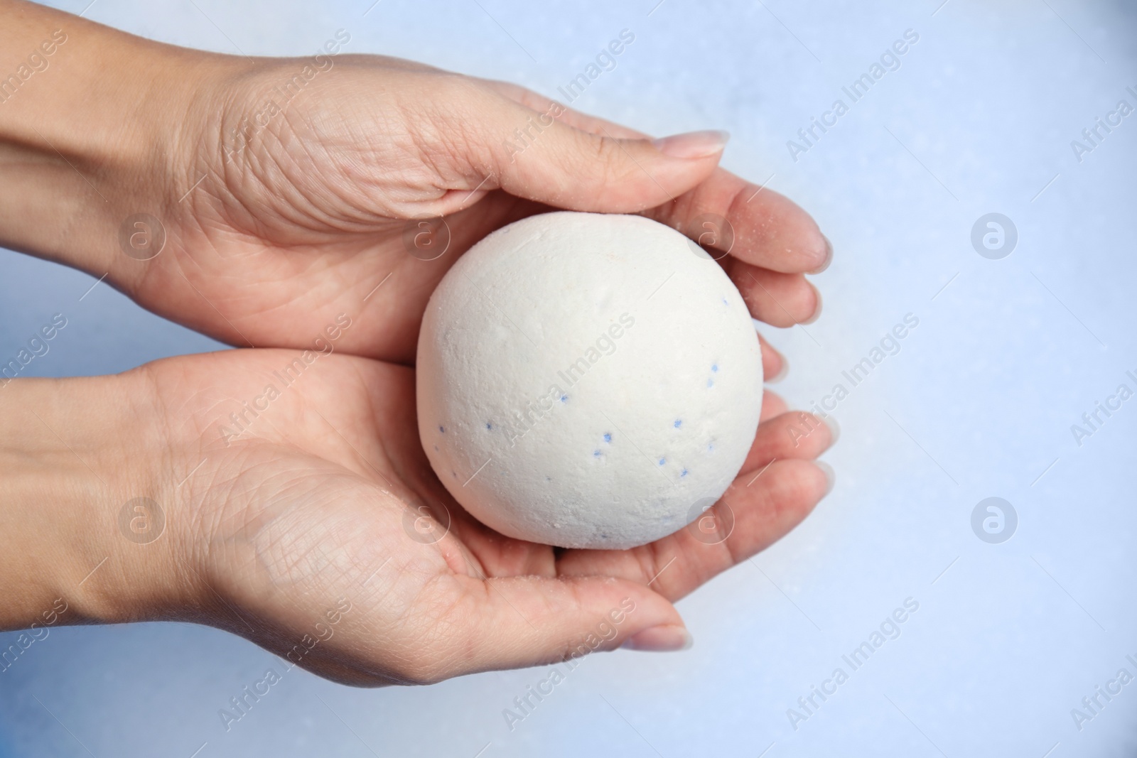 Photo of Woman holding bath bomb over foam, closeup