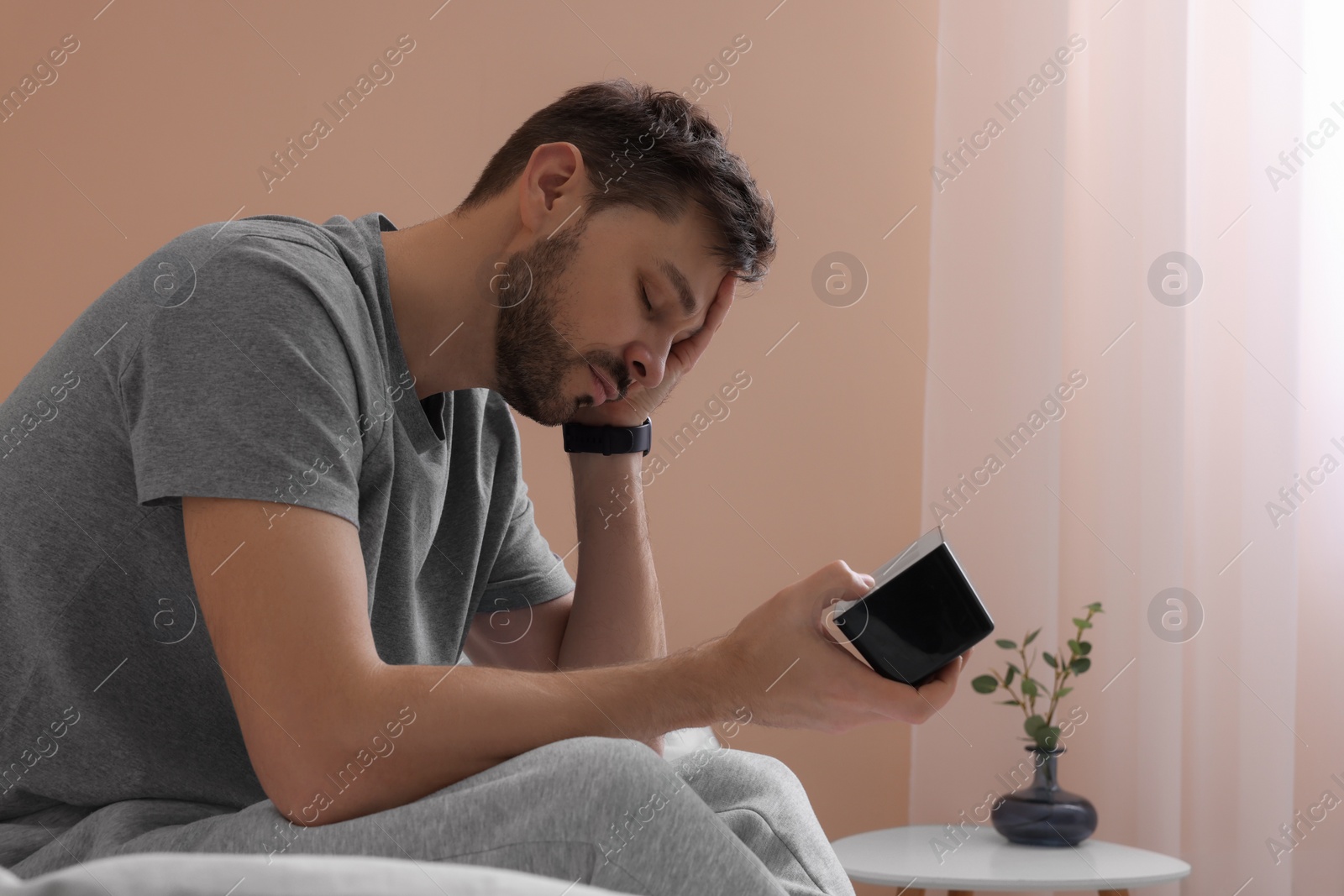 Photo of Sleepy man with clock in bed at home