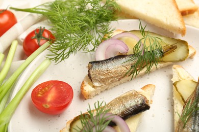 Photo of Delicious sandwiches with sprats, pickled cucumber, onion and dill served on plate, closeup
