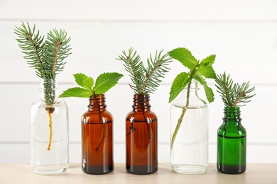 Photo of Glass bottles of different essential oils with plants on table