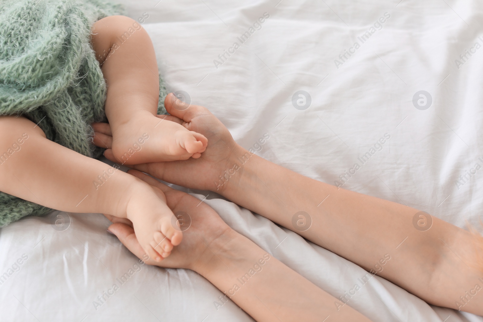 Photo of Mother holding feet of her little baby on bed, closeup