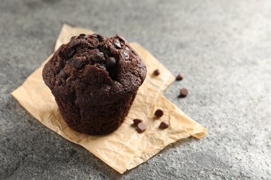 Photo of Delicious chocolate muffin on grey textured table, closeup. Space for text