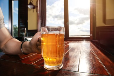 Photo of Man with glass of tasty beer at wooden table in pub, closeup