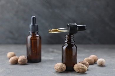 Photo of Bottles of nutmeg oil and nuts on grey table